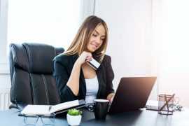 Forretningskvinne holder kredittkort foran bærbar pc
