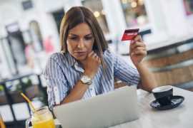 Ung kvinne holder opp et kredittkort mens hun ser på en pc-skjerm
