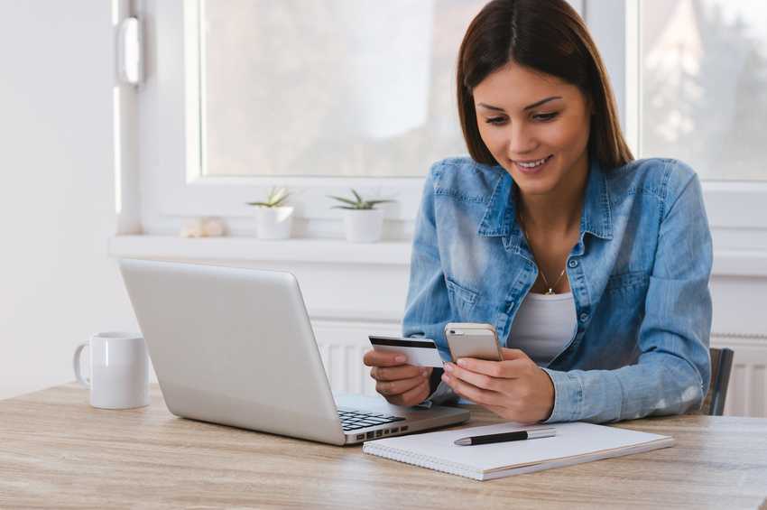 Ung kvinne studerer telefonen sin med kredittkort i hånden